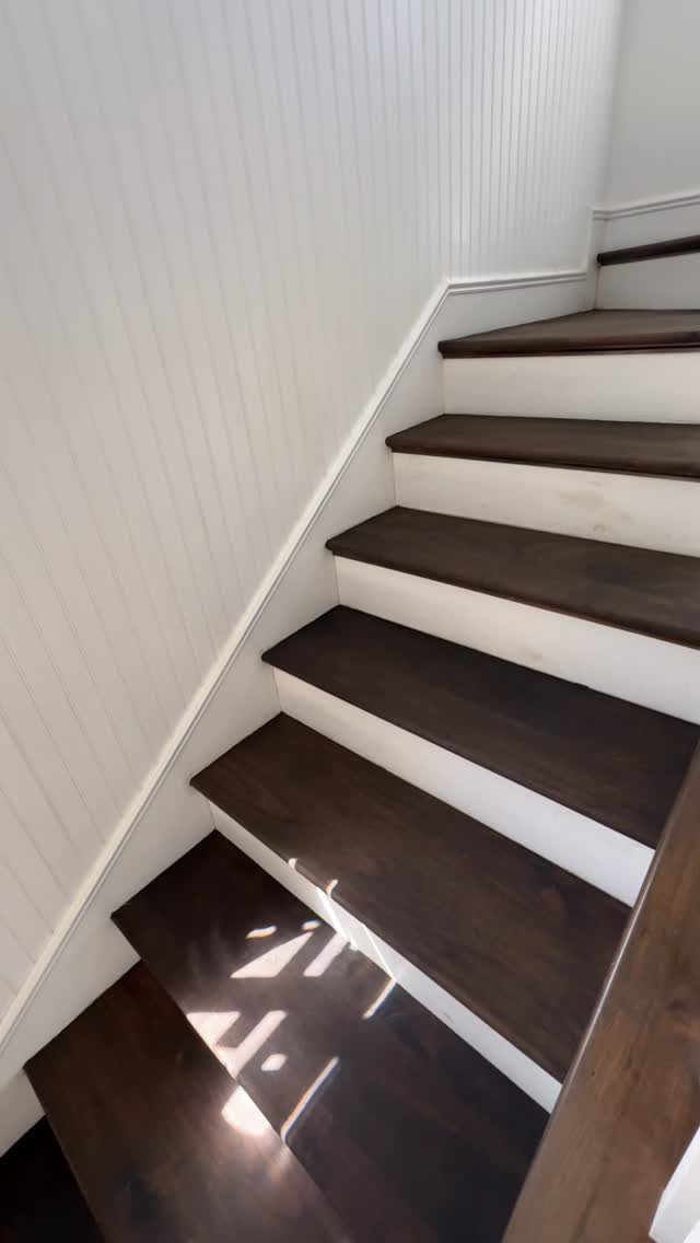 Dark espresso stained wooden stairs with white risers against a white beadboard wall.