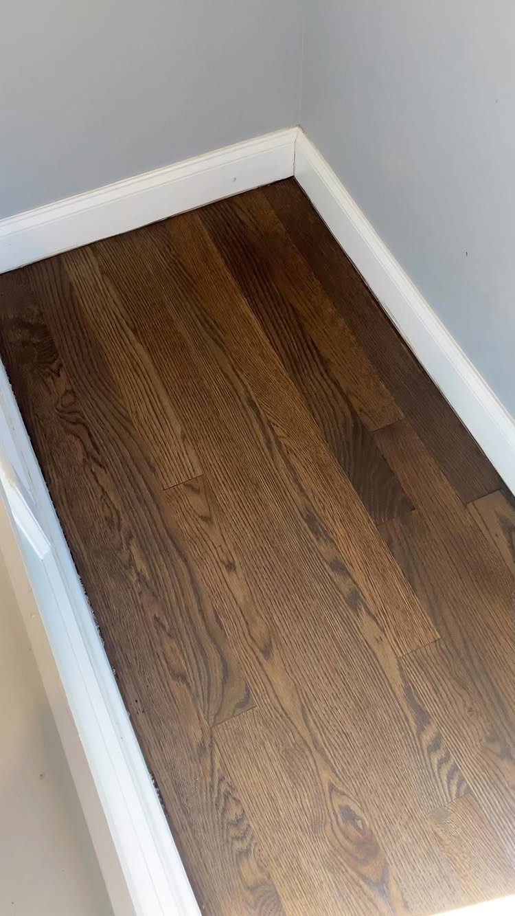 Dark brown wood floor planks with visible grain patterns installed against a gray wall.