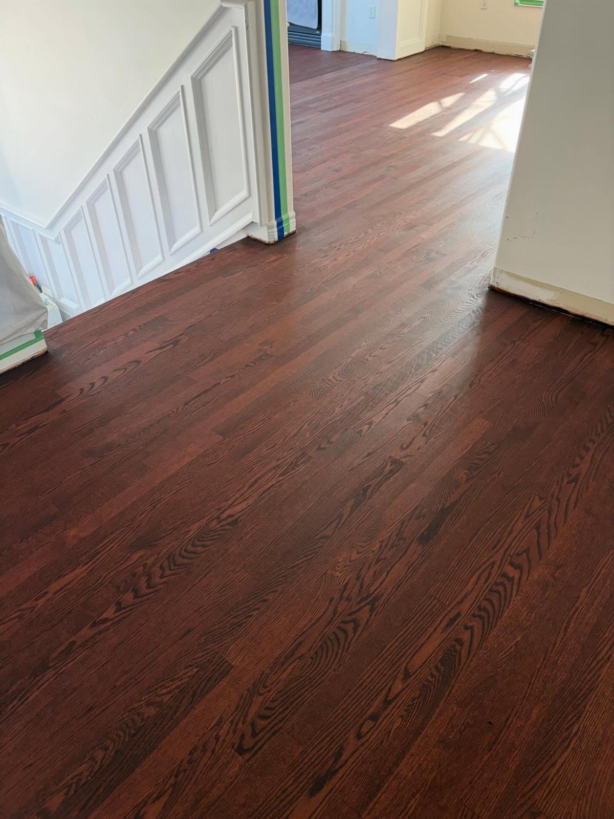 Reddish-brown stained hardwood flooring stretching across a room next to a white staircase.