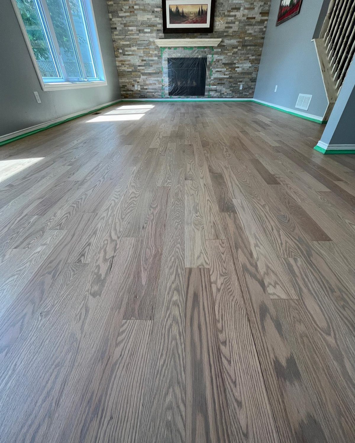 Light gray stained wood flooring in a room with a stone fireplace and gray walls.