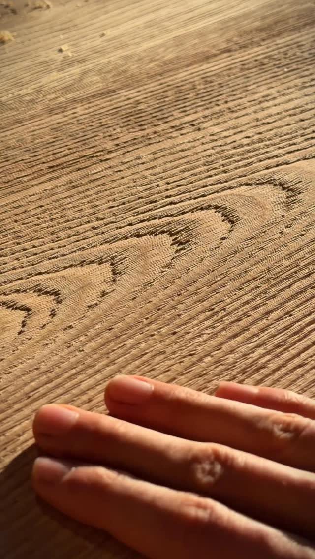 A hand touching the deep, textured grain of a light brown wooden surface.