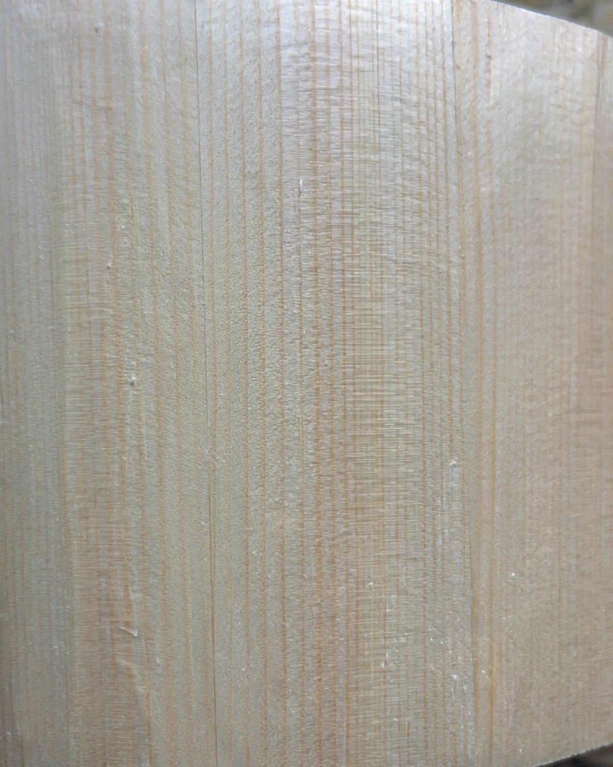 Light-colored wood surface showing fine vertical grain and subtle horizontal texture patterns.