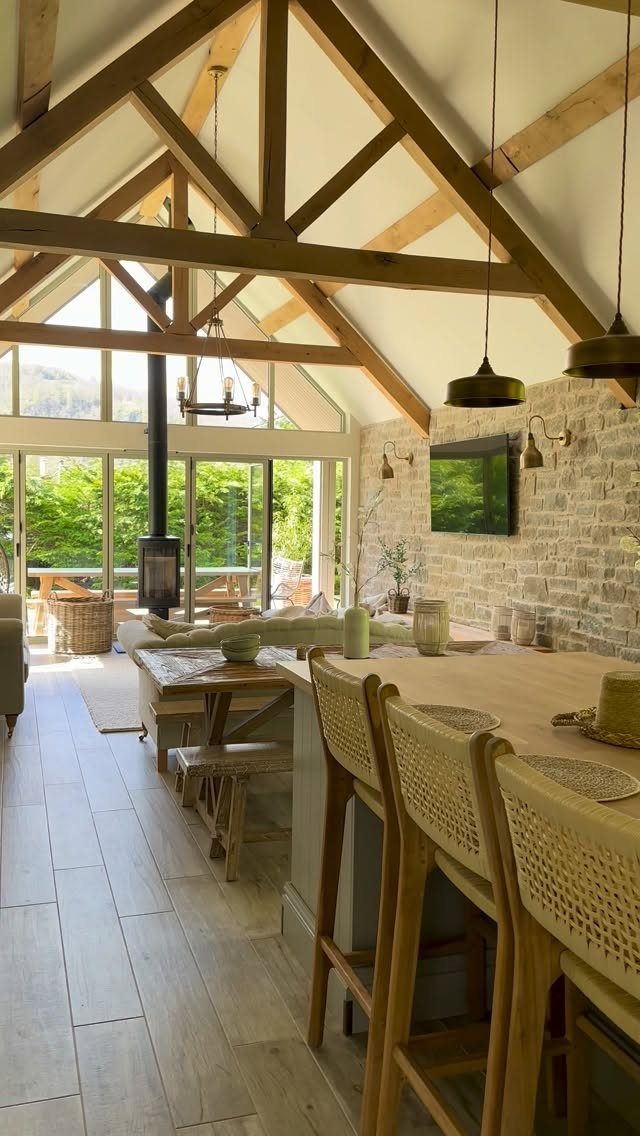 Light wooden plank flooring extends through a bright room with exposed timber beams and large glass doors.