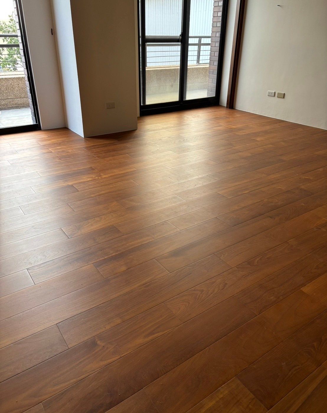 Polished medium-toned wooden plank flooring in a bright, modern room with white walls.