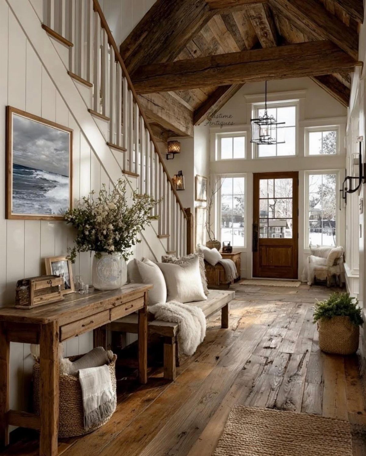 Wide rustic wooden floor planks in a bright, farmhouse-style entryway with a staircase and wooden furniture.